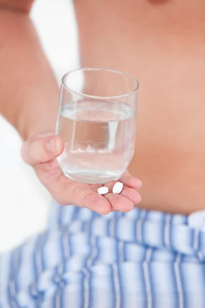 Primer plano de un hombre enfermo sosteniendo pastillas y un vaso de agua en su — Foto de Stock