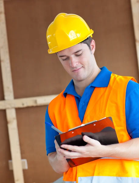 Handsome worker with hardhat taking notes on his clipboard — Stock Photo, Image