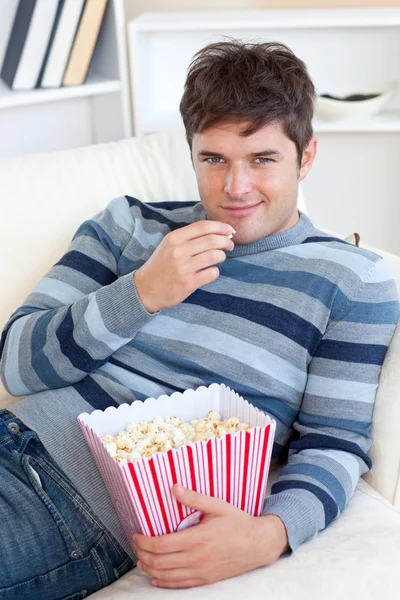 Красивый молодой человек ест попкорн лежа на диване — стоковое фото