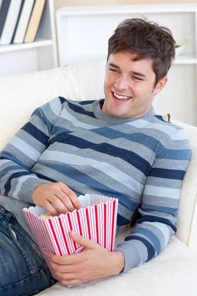 Cheerful young man eating popcorn lying on the sofa — Stock Photo, Image