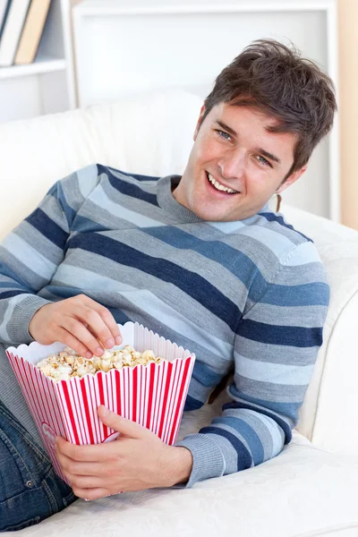 Zachwycony, młody człowiek jedzenie popcornu leżąc na kanapie — Zdjęcie stockowe