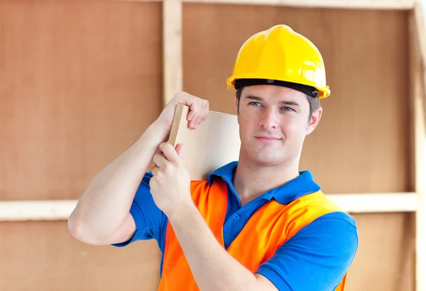 Assertivo jovem trabalhador do sexo masculino com um capacete amarelo carregando uma madeira — Fotografia de Stock