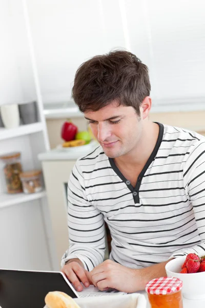 Светлый человек завтракает и использует свой ноутбук на кухне — стоковое фото