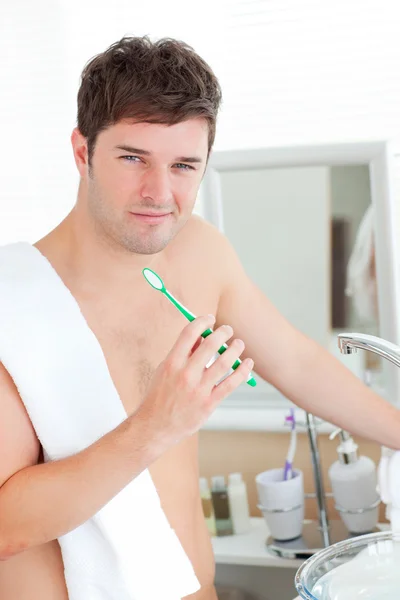Positive young man with a towel brushing his teeth in the bathro — Stock Photo, Image