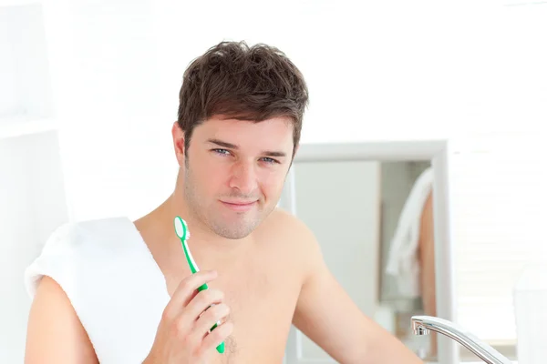 Smiling young man with a towel brushing his teeth in the bathroo — Stock Photo, Image
