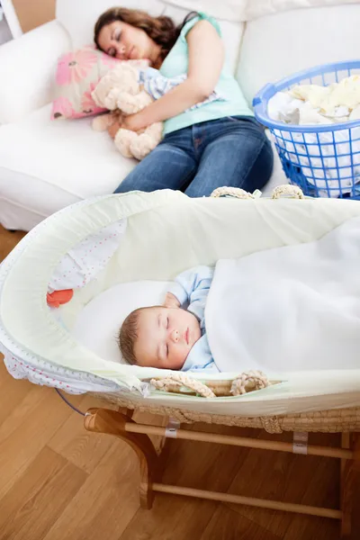 Joven madre durmiendo en el sofá mientras su bebé está durmiendo en —  Fotos de Stock