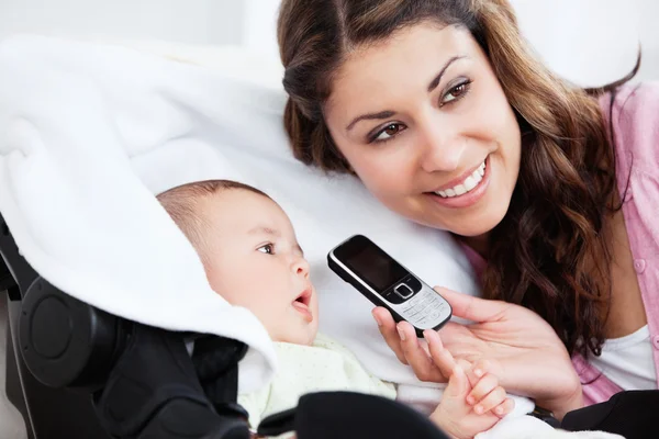 Lächelnde junge Mutter zeigt ihrem neugierigen Baby ein Zellophon — Stockfoto