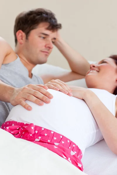 Radosny kaukaski kobieta w ciąży leżąc na łóżku z mężem — Zdjęcie stockowe