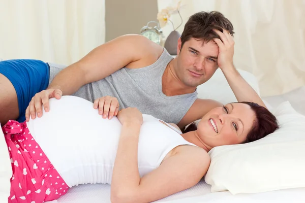 Счастливая белая беременная женщина лежит в постели со своим мужем — стоковое фото