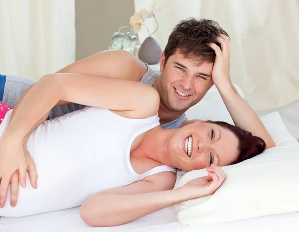 Смеющаяся белая беременная женщина, лежащая в постели со своим мужем — стоковое фото