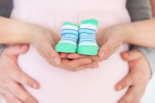 赤ちゃんの靴を保持している妊娠中の女性と彼女の husba のクローズ アップ — Stockfoto