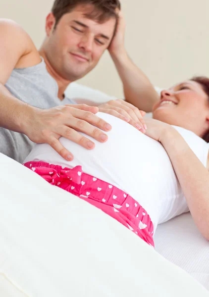 Счастливая беременная женщина лежит в постели со своим мужем — стоковое фото