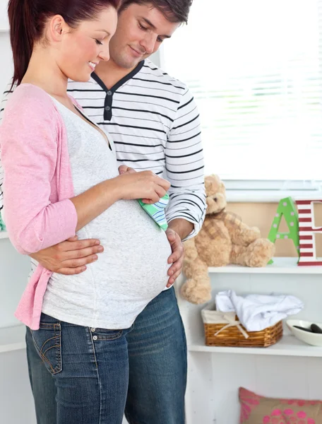Sorrindo mulher grávida segurando sapatos de bebê enquanto marido tocando — Fotografia de Stock
