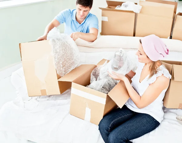 Happy young couple unpacking boxes with glasses — Stock Photo, Image