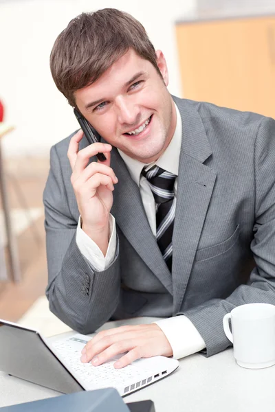 Charismatische zakenman met behulp van zijn laptop tijdens het gesprek op de telefoon — Stockfoto