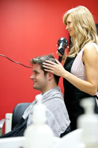 Cabeleireiro loiro secando o cabelo de seu cliente — Fotografia de Stock