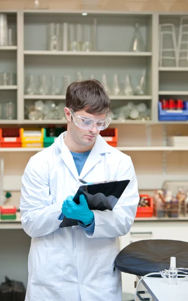 Científico masculino concentrado escribiendo en un portapapeles — Foto de Stock