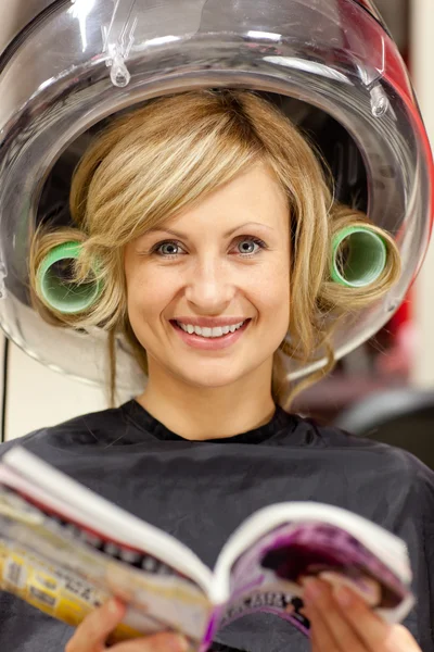 Mujer encantada leyendo una revista con rizadores de pelo bajo un hai —  Fotos de Stock
