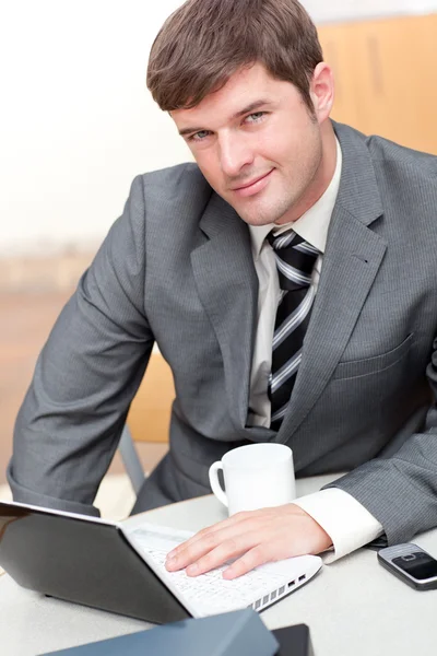 Upptagen affärsman med en bärbar dator, en mobiltelefon och en mugg som sitter vid — Stockfoto
