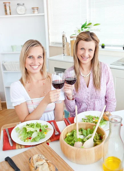 Hermosas mujeres tintineo vasos y comer ensalada sentado en el — Foto de Stock