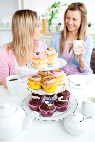 Dois amigos bonitos comendo cupcakes sentados na cozinha em casa — Fotografia de Stock