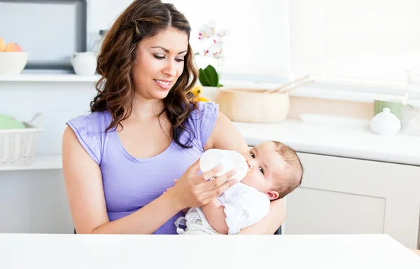 Cute mother feeding her baby siiting in the kitchen — Stock Photo, Image