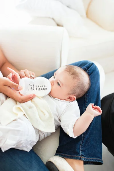 Close-up de uma mãe dando leite ao bebê sentado no sofá — Fotografia de Stock