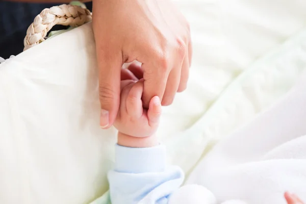 Close-up de uma jovem mãe segurando a mão de seu bebê deitado em — Fotografia de Stock