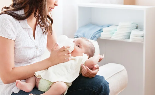 Close-up of a proud mother bottle-feeding her baby sitting in th — Stock Photo, Image