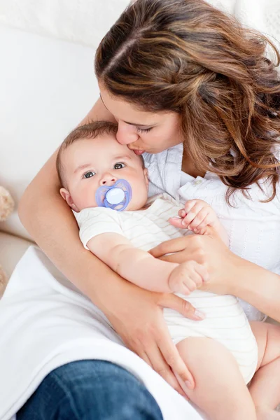 Adorable young mother kissing her baby sitting on a couch — Stock Photo, Image