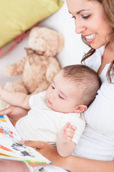 Portrait of joyful mother reading a book to her baby sitting in — Stock Photo, Image