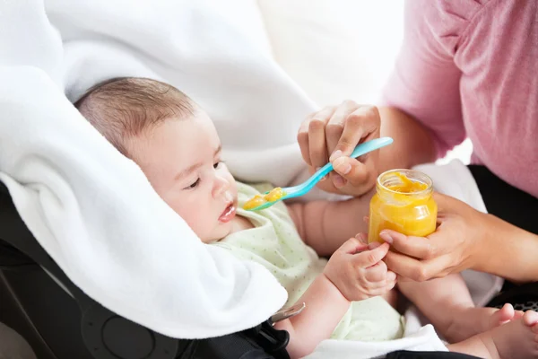 Close-up de uma jovem mãe dando purê de cenoura para seu bebê para l — Fotografia de Stock