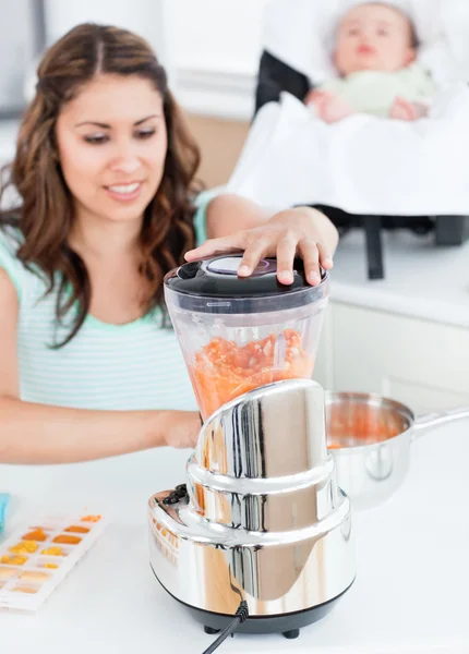 Schöne Mutter mixt Karotte mit einem Mixer für ihr Baby-Mittagessen — Stockfoto