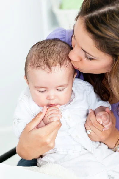 Retrato de uma mãe adorável beijando seu bebê iin a cozinha — Fotografia de Stock