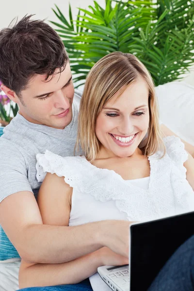 Mujer alegre usando un portátil acostado en el sofá con su novio — Foto de Stock