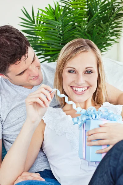 Mujer feliz desenvolviendo un regalo acostado en el sofá con su novio — Foto de Stock