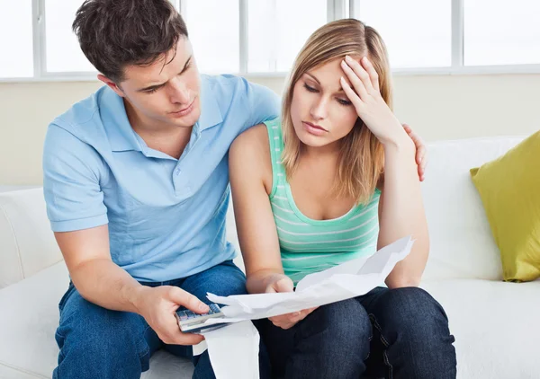Беспокойная женщина смотрит на счета со своим парнем, держащим калькулятор — стоковое фото
