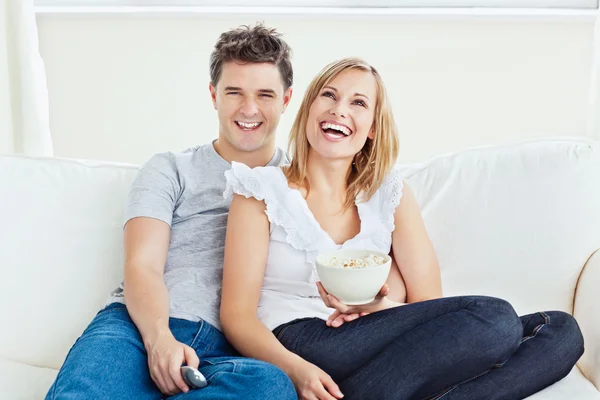Alegre pareja viendo una película con pop-corn sentado en el sofá — Foto de Stock