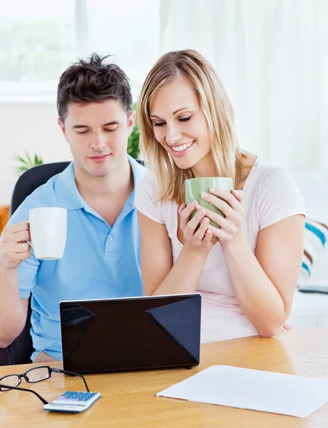 Happy couple using a laptop sitting together at a table holding — Stock Photo, Image