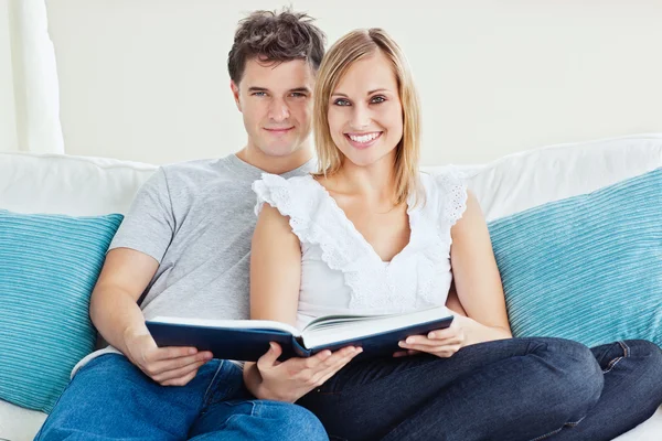 Cute couple reading a book together sitting on the couch at home — Stock Photo, Image