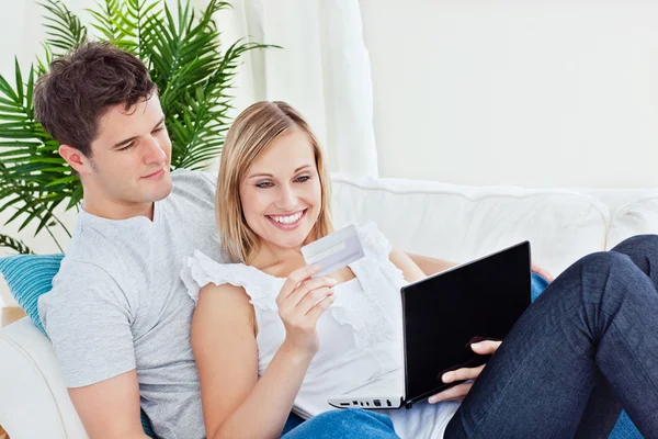 Счастливая пара с кредитной картой и ноутбуком отдыхает на диване — стоковое фото