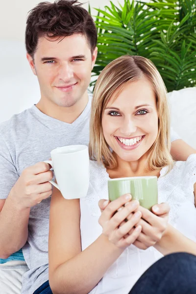 Krásný pár, spočívající na pohovce, drží šálků kávy — Stock fotografie