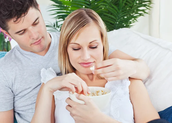 Retrato de um casal caucasiano relaxante no sofá e comer p — Fotografia de Stock