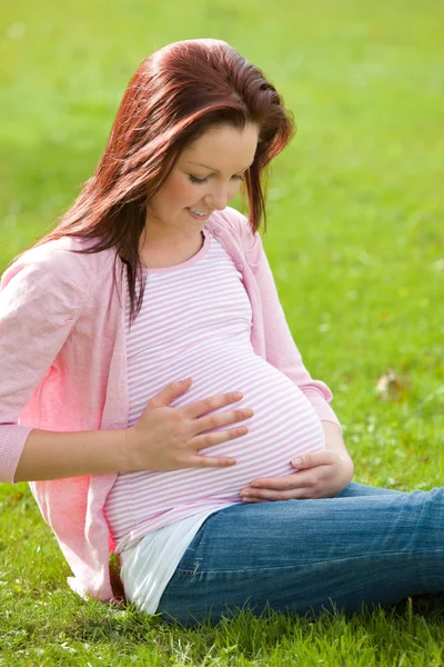 Çok güzel hamile kadın göbeğine dokunmayı çimlerde oturan — Stok fotoğraf