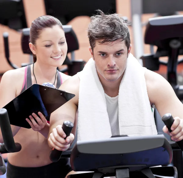 Smart female coach taking notes while her pupil is pedaling on a — Stock Photo, Image