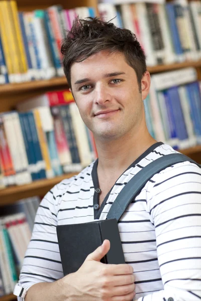 Portrait of a smart student holding a book standing in the libra — Stock Photo, Image
