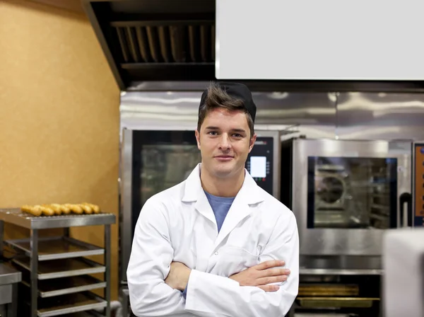 Cheerful baker standing in his kitchen with baguettes and stove — Stock Photo, Image