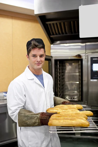 Happy baker showing his baguettes to the camera standing in his — Stock Photo, Image