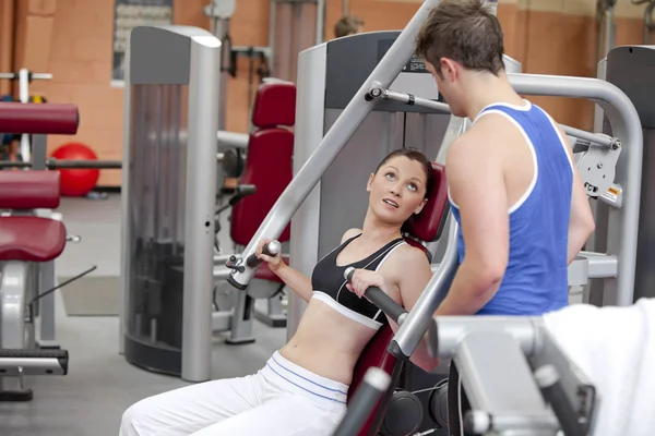 Sportliche Frau sitzt auf einer Schulterpresse und spricht mit ihrem Trainer — Stockfoto