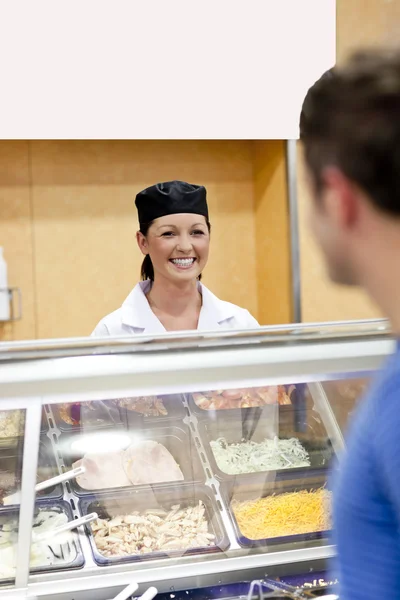 Joyful baker behind her display and customer in the queue talkin — Stock Photo, Image